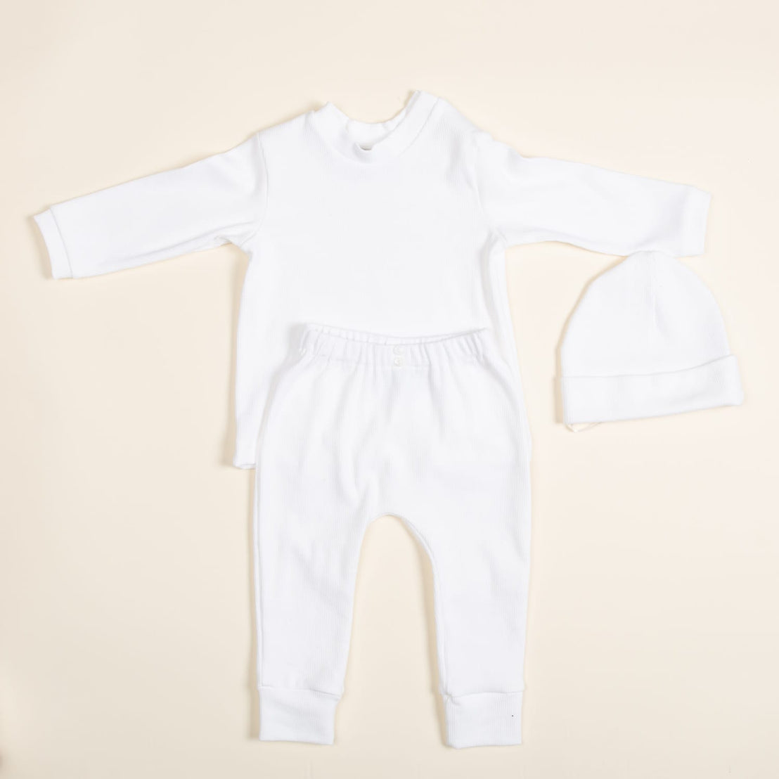 Introducing the Ivory Pima Top & Leggings set, a handcrafted baby outfit from the USA. This ensemble, featuring a long-sleeved top, matching leggings, and a cozy hat is crafted from soft Pima cotton. Arranged on a light background, it presents a simple yet elegant minimalist design.