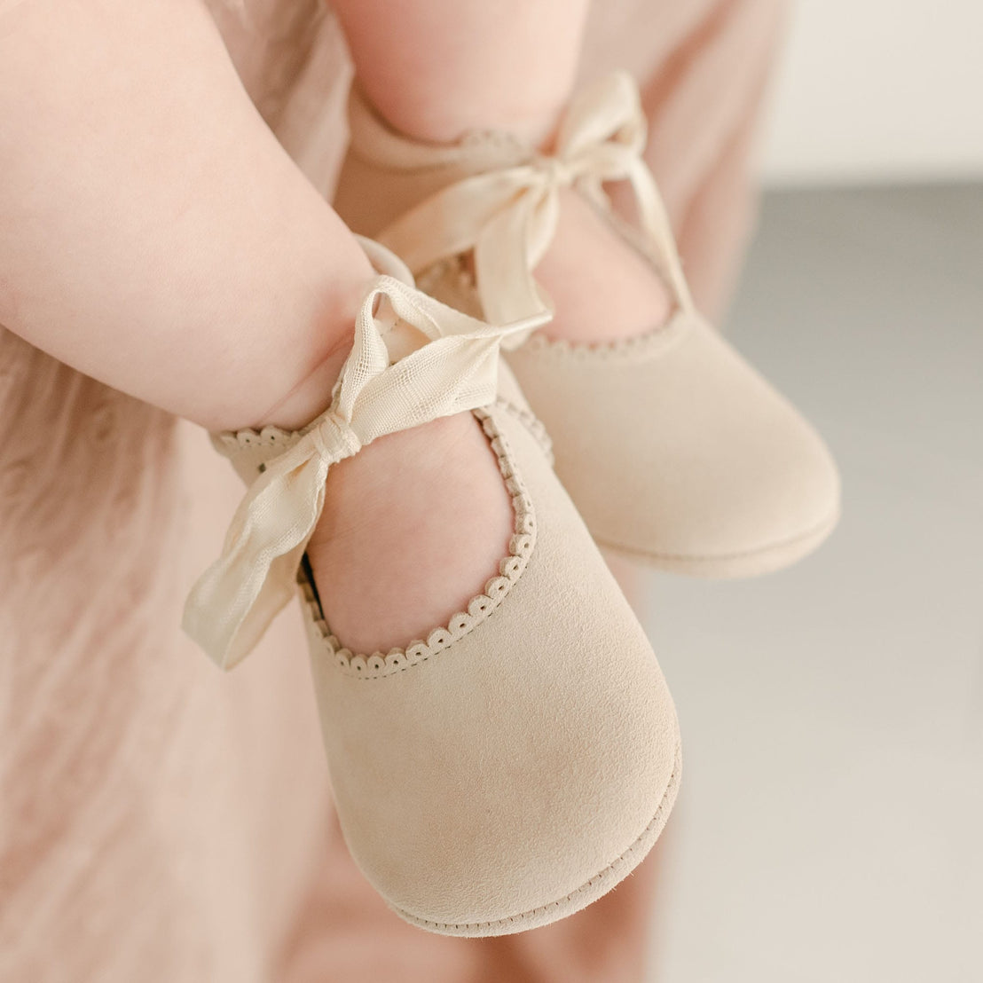 Close-up of a child's feet wearing Kristina Tie Mary Janes with satin ribbons, against a soft pink fabric background, perfect for baptism and vintage-inspired heirloom photography.