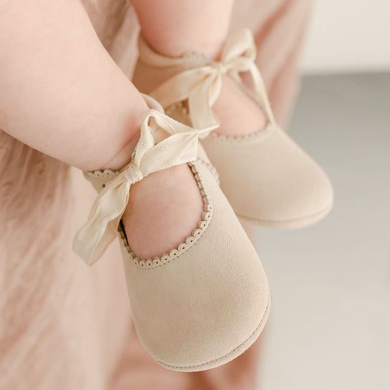 Close-up of a child's feet wearing Kristina Tie Mary Janes with satin ribbons, against a soft pink fabric background, perfect for baptism and vintage-inspired heirloom photography.