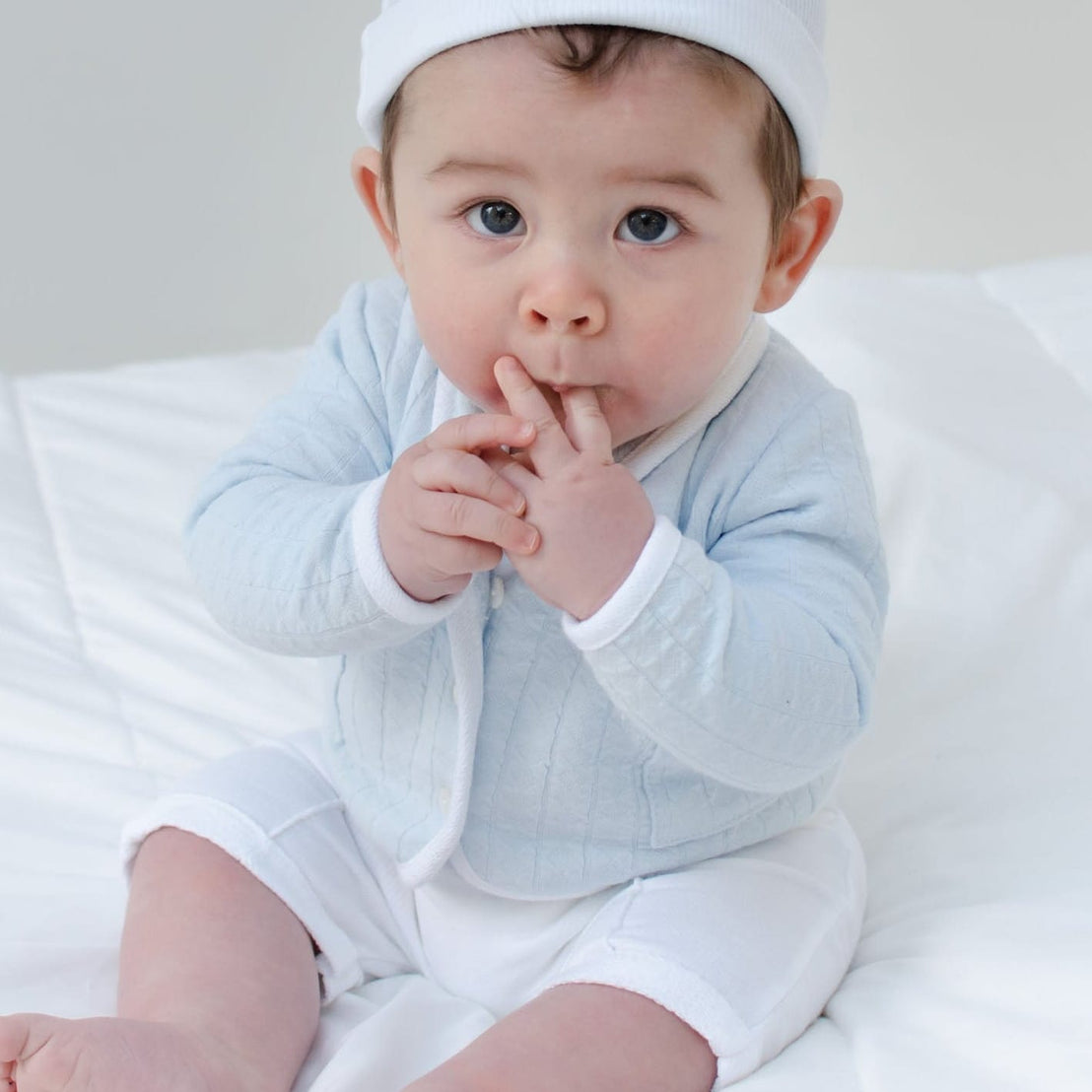 Baby boy sitting on the ground and wearing the Logan 3-Piece Shorts Suit (with matching White Ribbed Cotton Beanie).