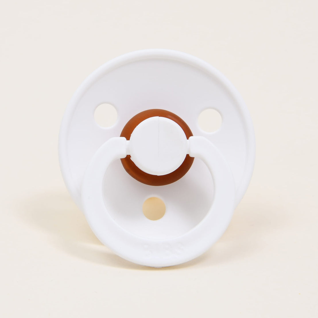 A Mason Pacifier in White positioned straight on, against a light beige background. The pacifier features a rounded handle and circular shield with ventilation holes.