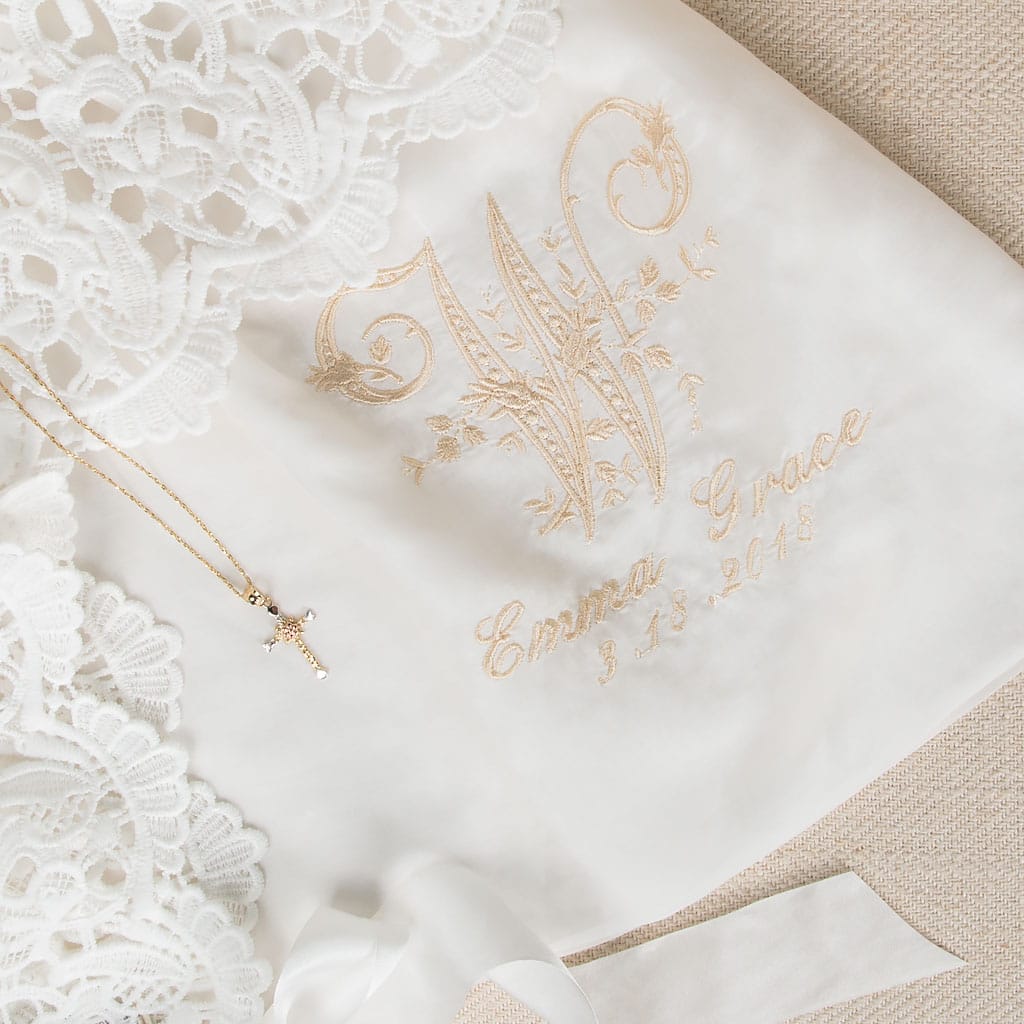 Close-up of the monogram on the Lola gown, featuring a detailed embroidered 'W' initial, with the name 'Emma Grace' and the date '3-13-2018,' showcasing personalization options for christening or birth.