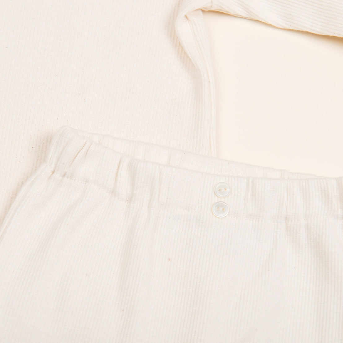 A close-up of the Natural Ivory Ribbed Cotton Top & Leggings, showcasing the cream-colored ribbed texture. The pants feature an elastic waistband with two small white buttons, paired with a matching long-sleeve top. Handmade in the USA, this outfit material looks wonderfully soft and comfortable.