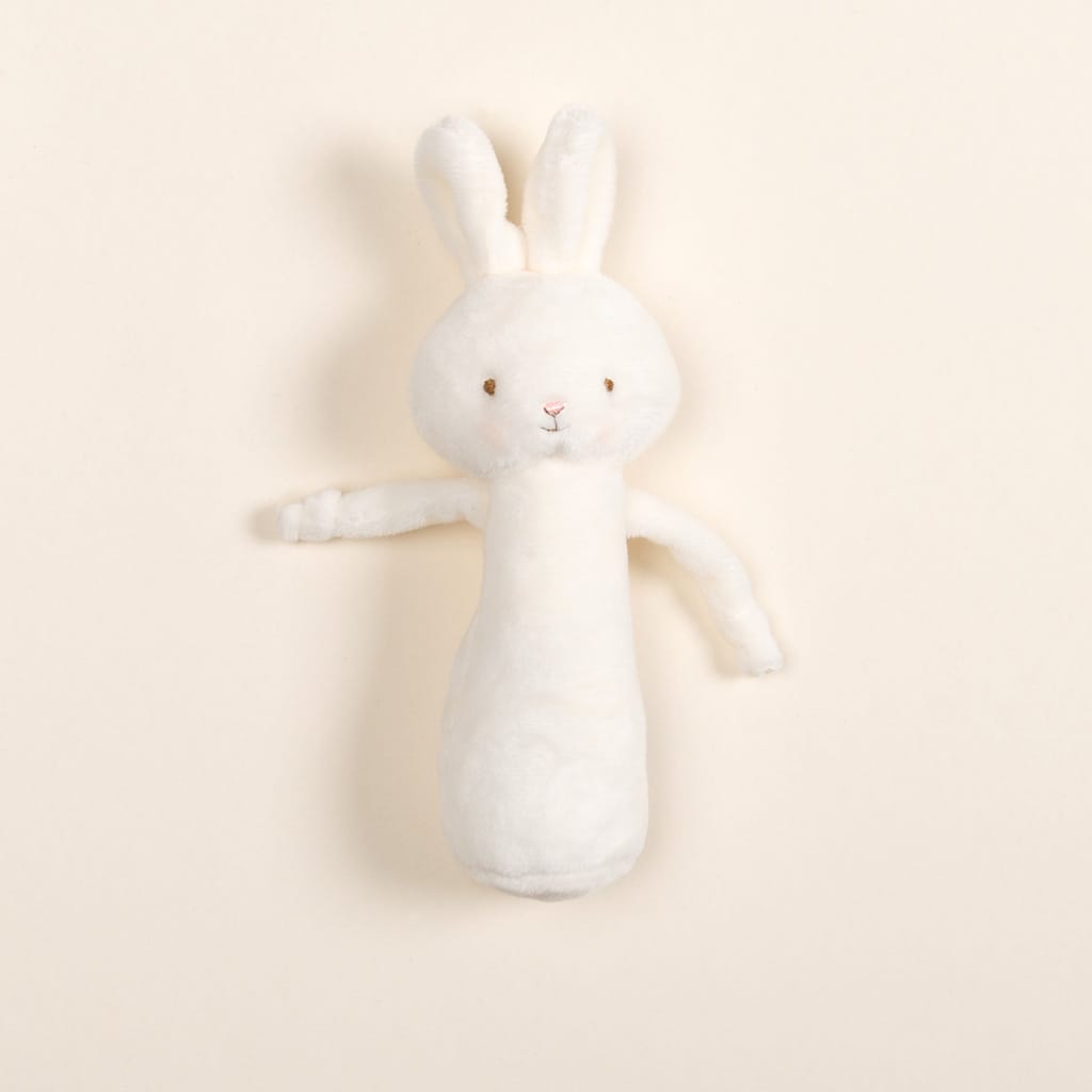 A soft, plush toy designed as a white bunny with floppy ears and stitched eyes and mouth rests against a plain, light cream background. The Plush Chime Rattle is baby-safe with a gentle chime inside and is wrapped in delicate baby blue velour for an added touch of charm.