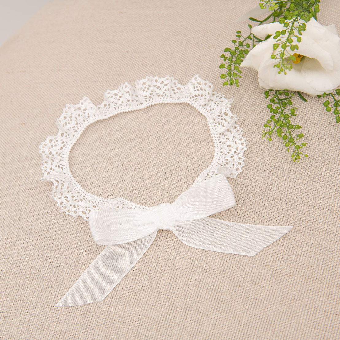 Close-up of the Poppy Headband displayed on a beige surface, featuring a delicate white bow and intricate lace trim.