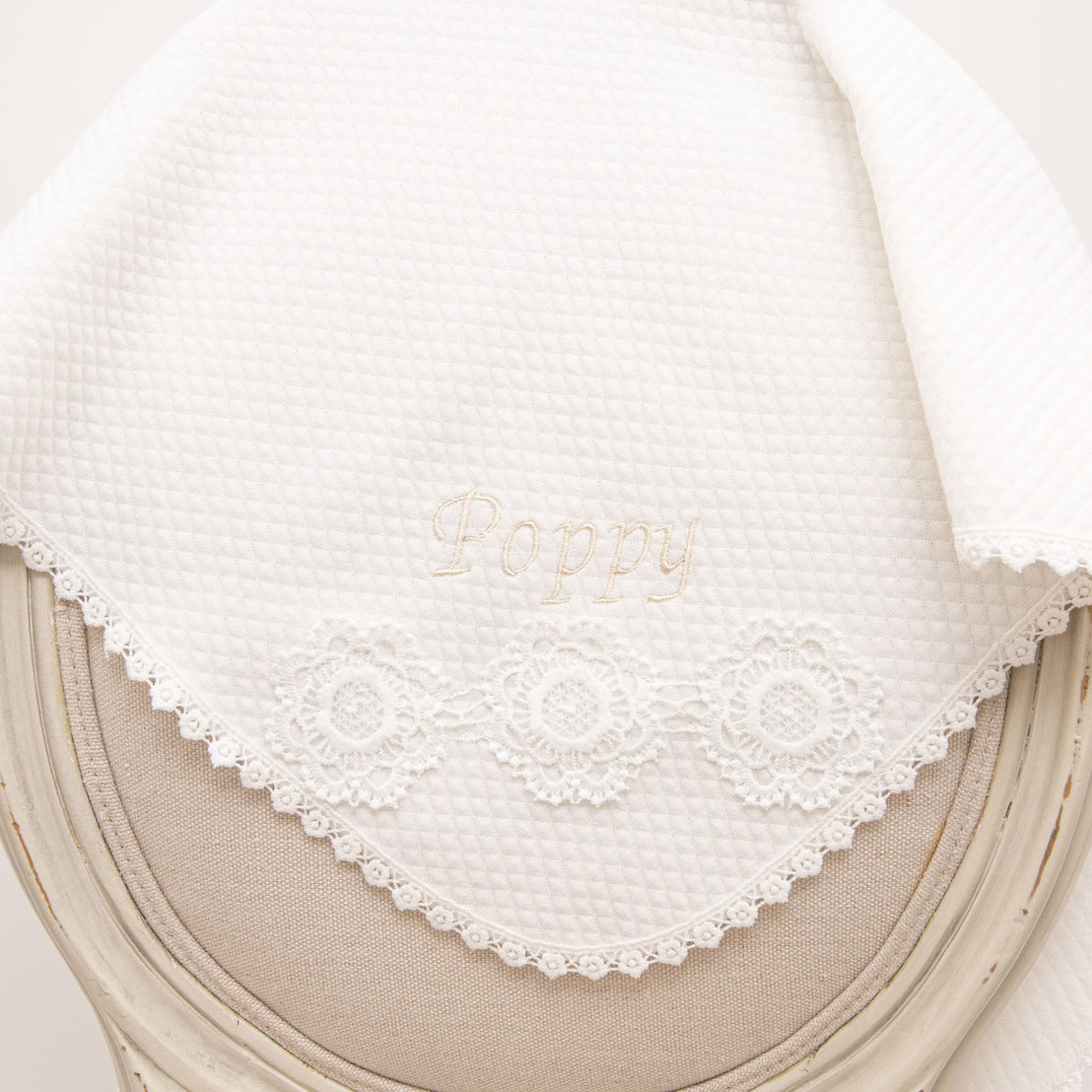 Poppy Personalized Blanket draped over a chair, featuring embroidered 'Poppy' lettering, floral lace detailing, and soft quilted fabric.