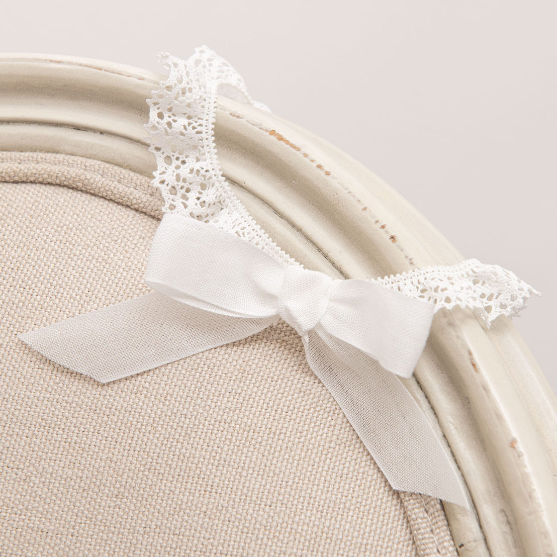 Close-up of the Poppy Headband displayed on a vintage chair, featuring a delicate white bow and intricate lace trim.