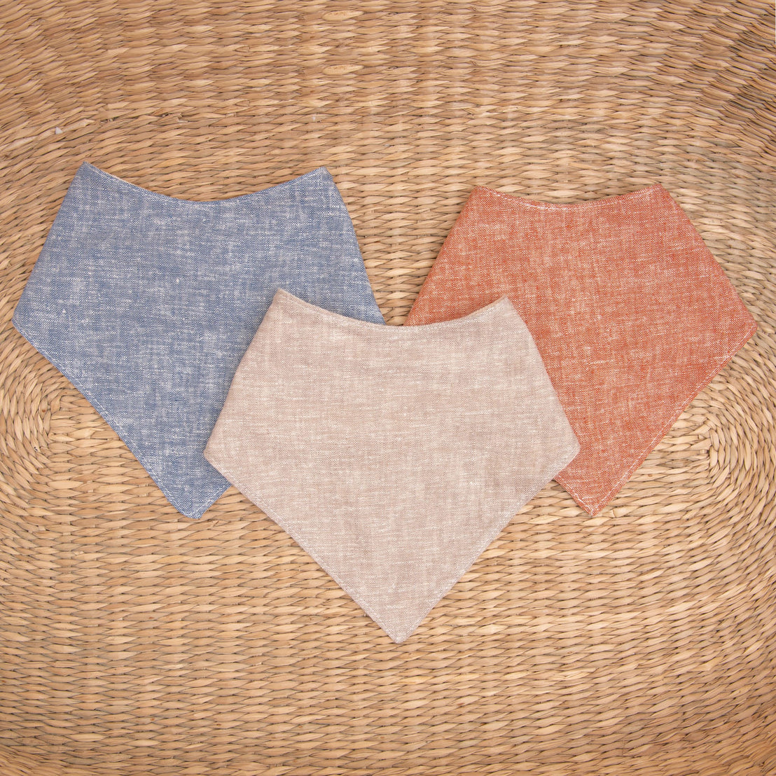 Flat lay photo of all three colors of the Silas Bandana Bib. The bibs are made from linen in three different colors: indigo, sand, and clay.