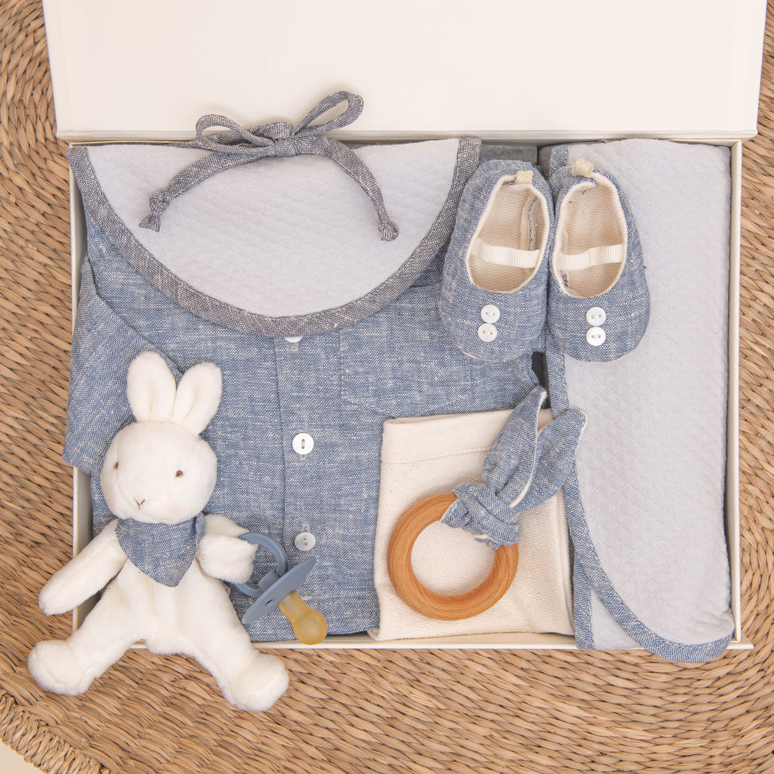 Photo of the indigo colored Silas Gift Set in a Gift Box. Included in the box is the shirt, pants, booties, bib, teether, bunny, pacifier, and personalized blanket.