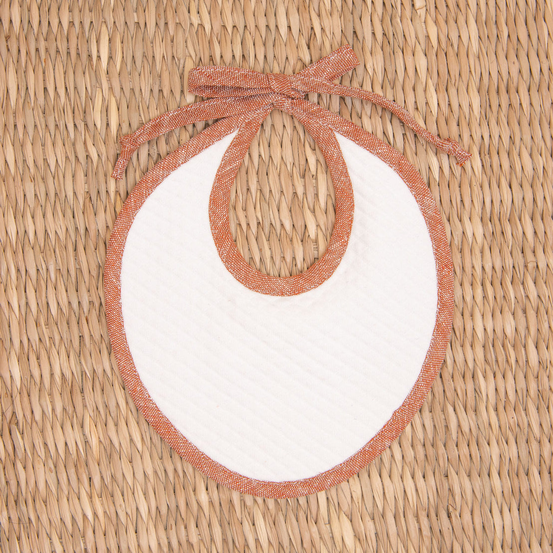 Flat lay photo of the red Silas Linen Trim Bib. The bib is made from textured cotton in light ivory