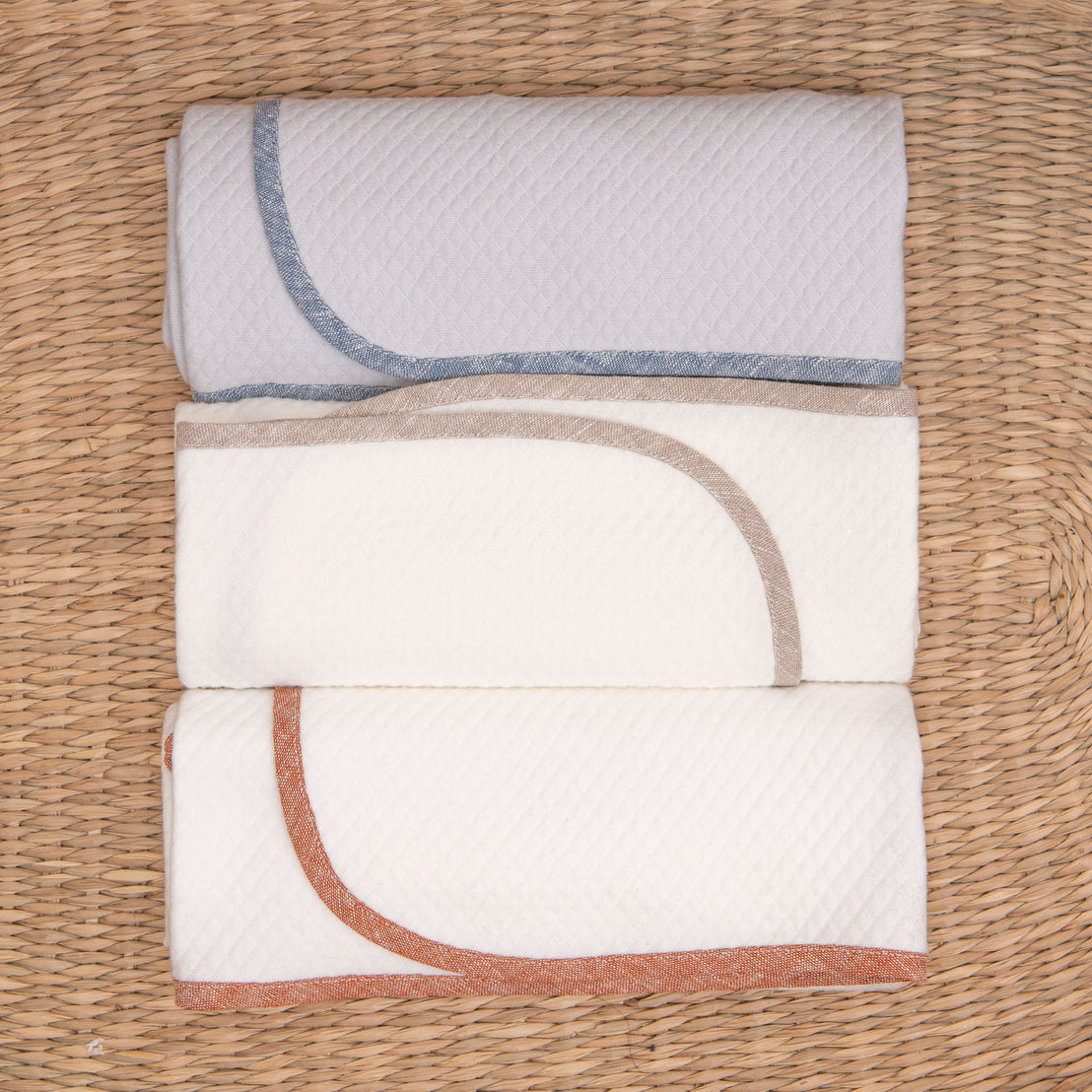Photo of all three colors of the Silas Personalized Blanket in a woven basket. The three colors include clay, indigo, and sand