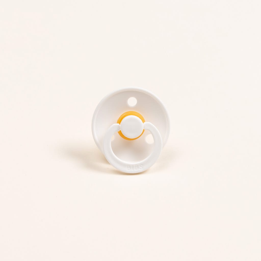 The Silly Bunny Buddy & Pacifier, featuring a sleek white design with a small yellow ring and smooth, round base, sits elegantly against the plain off-white background, making it an ideal baby gift.