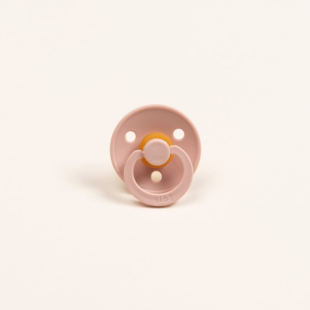 The Silly Bunny Buddy & Pacifier, in pink with a round shield and amber-colored nipple, stands upright on a white background. It features two ventilation holes and an embossed brand name on the handle. Ideal as a baby gift, this delightful accessory pairs perfectly with any pacifier holder for added convenience.