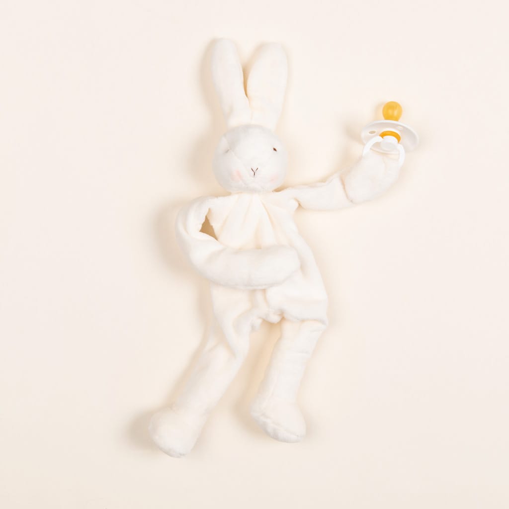 The Silly Bunny Buddy & Pacifier, perfect as a baby gift, features a white plush rabbit cradling a yellow pacifier. Soft and floppy with long ears and stitched facial features, this adorable companion lies against a plain, light background.