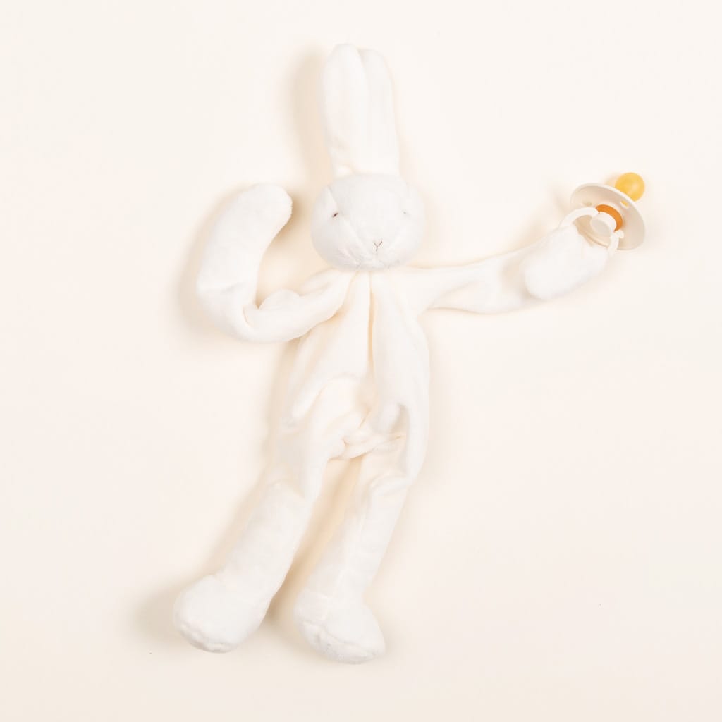 A Silly Bunny Buddy pacifier holder with long ears and limbs, perfect for a baptism, on a pale cream background.