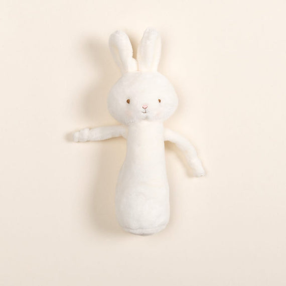 Introducing the White Bunny Chime Rattle: a sweet companion crafted from baby-safe materials, this plush toy rabbit showcases floppy ears and a simple embroidered face. Its soft, elongated white velour body rests elegantly against a light beige backdrop, capturing a nostalgic charm.