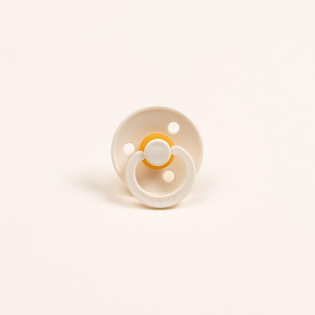 A bibs pacifier set in ivory, featuring the name Bibs on the handle. Set against a light backdrop. 