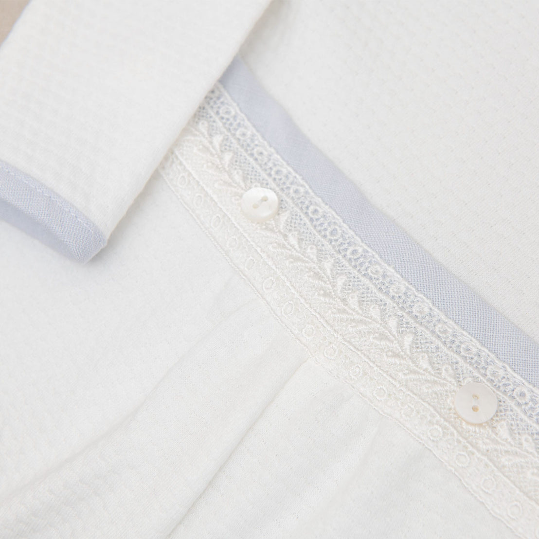 Close-up of the Harrison Long Sleeve Romper waistband, highlighting its lace embroidery, buttons, and soft blue trim.