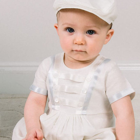 Baby boy sitting down and wearing the Owen Newsboy Cap and matching Linen Romper featuring silk ribbon in ivory and light blue across the front bodice and sleeves