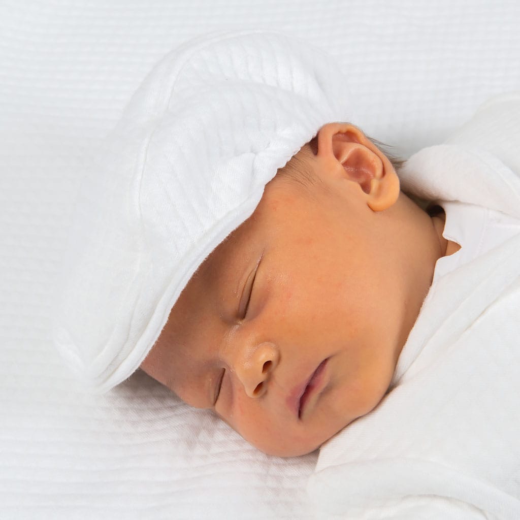A sleeping baby, wrapped in a white blanket and wearing a cozy cap, rests peacefully on a soft surface in their charming Elijah Newborn 3-Piece Suit.