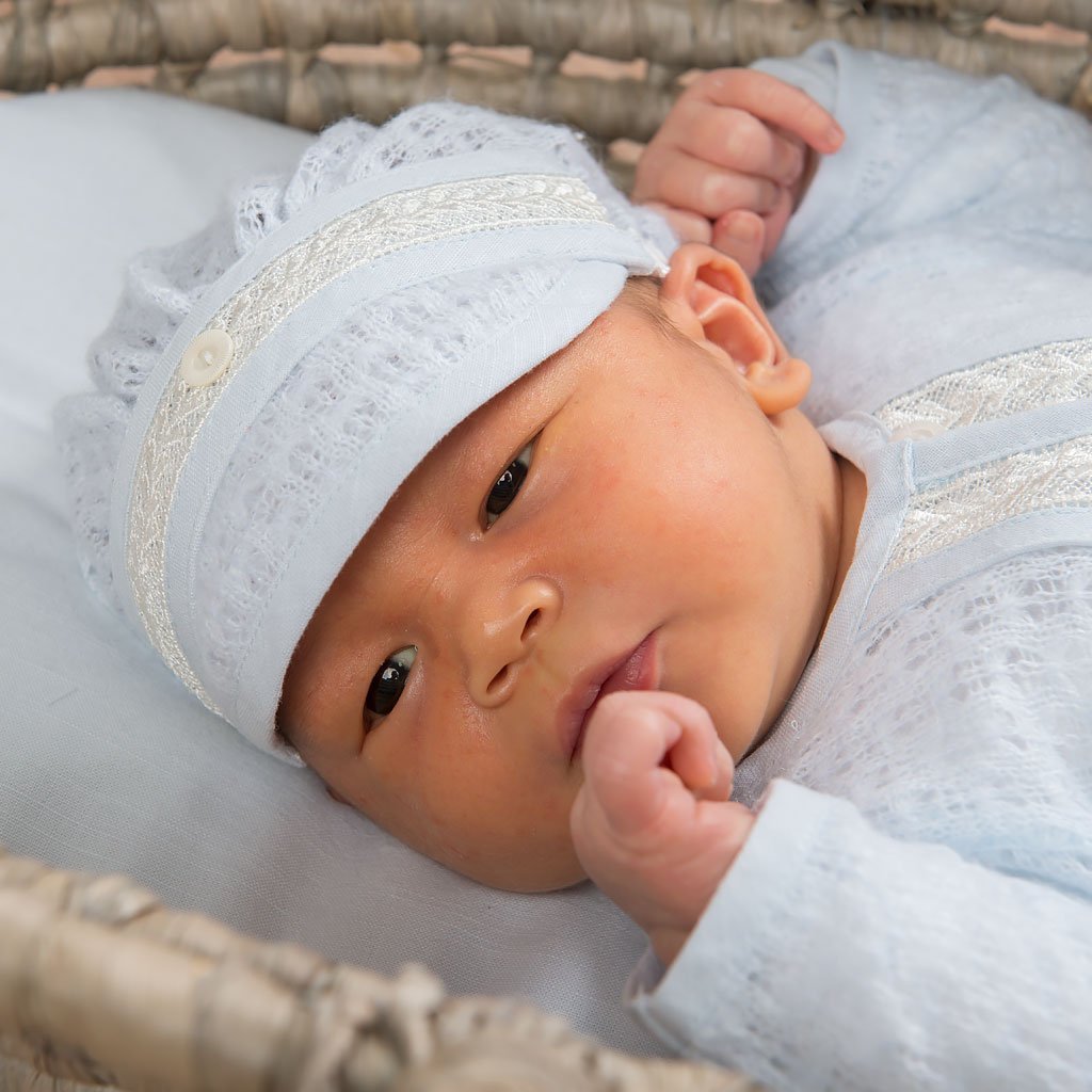 Newborn resting in a basket, dressed in the Harrison Newborn Knit Hat and sweater, highlighting the airy blue knit and delicate embroidered accents.