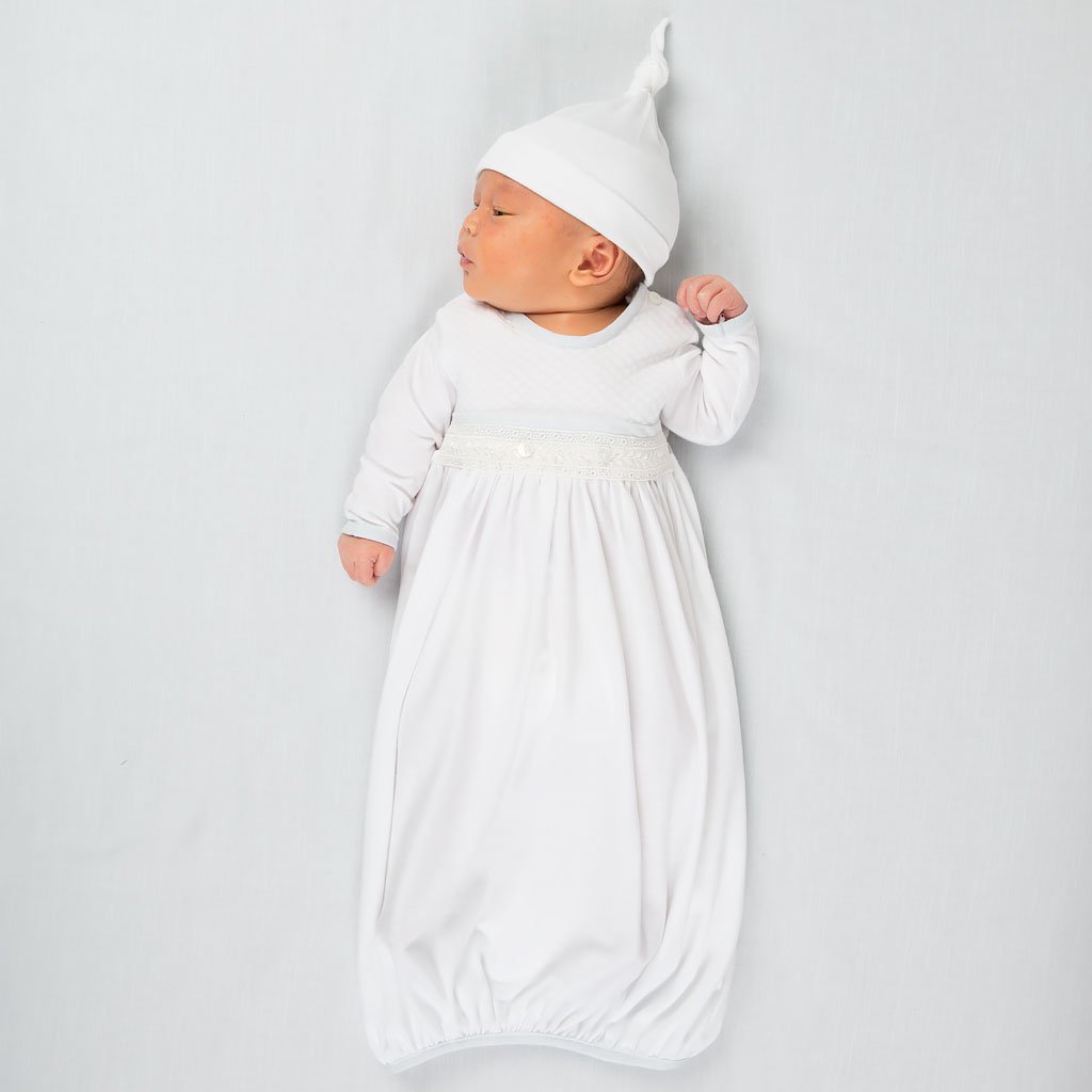 Photo of a newborn baby wearing a Harrison Knot Cap made with premium soft pima cotton in white with a knot design on top. He is also wearing Harrison Newborn Gown